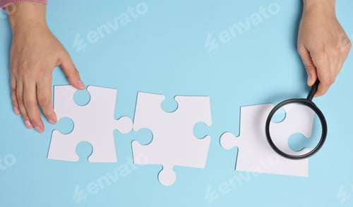 Preview: White empty puzzles and a magnifying glass in hand on a blue background, top view