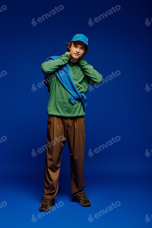 Preview: Stylish young man showcases contemporary fashion against a vibrant blue backdrop