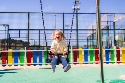 Preview: Happy baby girl enjoying swinging at playground on sunny day