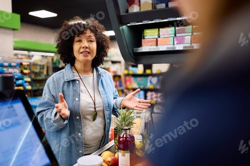 Preview: Mature woman talking to a cashier at supermarket checkout.