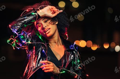 Preview: Portrait of a beautiful young woman with christmas lights looking at camera