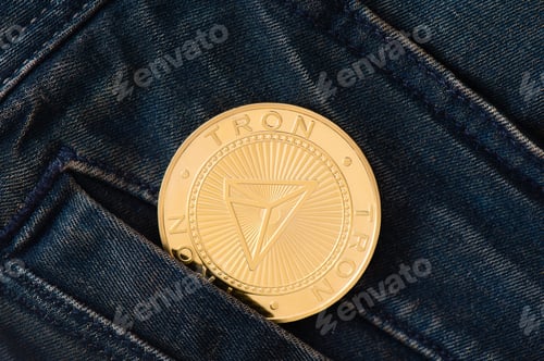 Preview: A golden physical TRON coin sticks out of the pocket of blue jeans close-up.