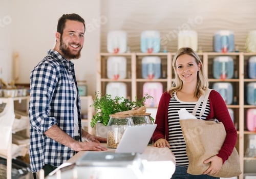 Preview: Young shop assistant serving an attractive woman in a zero waste shop.