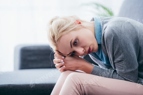 Preview: selective focus of upset woman with folded hands sitting at home