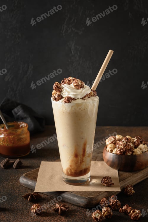 Preview: Banana and caramel milkshake garnished whipped cream and popcorn on dark.