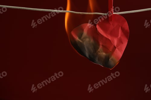Preview: Crumpled red paper heart burning on rope against burgundy background, space for text. Broken heart