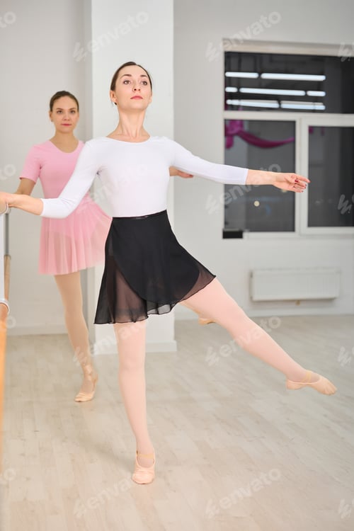 Preview: Two young female ballerinas practicing at ballet barre in bright studio