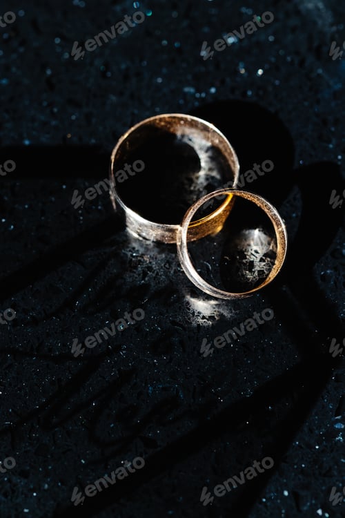 Preview: Two golden wedding rings shining on black marble surface