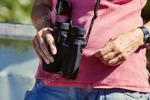 Preview: Midsection of man holding binoculars while standing outdoors