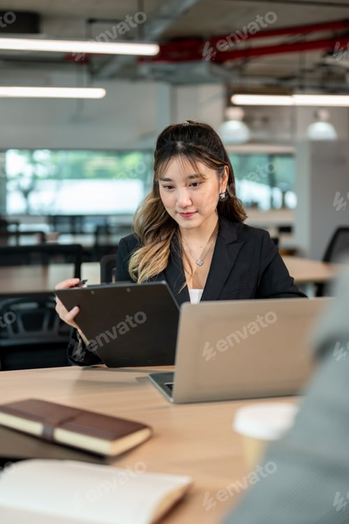 Preview: Businesswoman holding clipboard aside laptop sitting across coworker at wooden table in meeting room