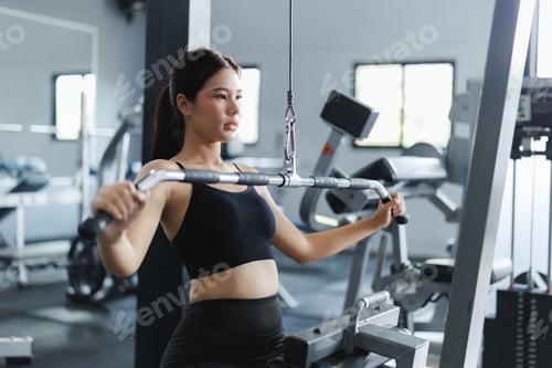 Preview: Asian woman doing back exercise with lat pulldown machine in gym