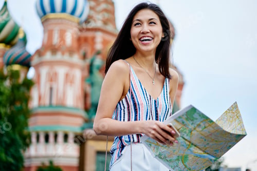 Preview: Funny Asian female tourist holding travel map and rejoicing while exploring historic center