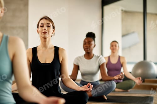 Preview: Young athletic woman meditating in lotus pose during Yoga class at health club.
