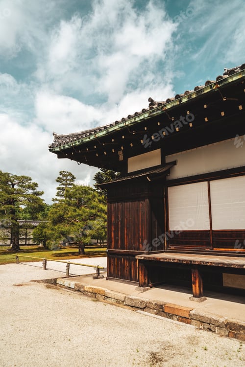 Preview: Wooden park bench situated in a grassy area surrounded by trees at the corner of a building.