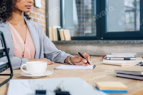 Preview: cropped view of african american Casual businesswoman writing in notebook at table in loft office