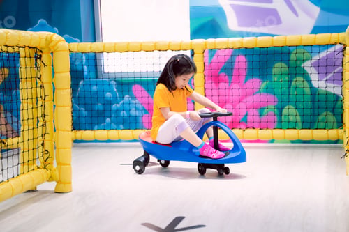 Preview: A child is having fun playing with a blue toy car, a cute Asian girl plays in an indoor playground.