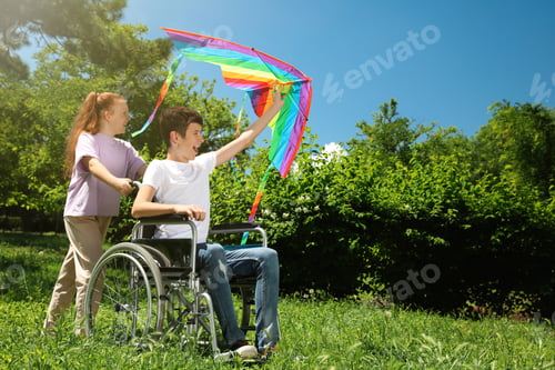 Preview: Happy teenage boy in wheelchair with kite and girl at park on sunny day