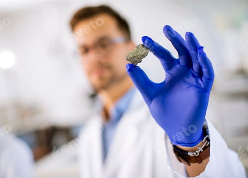 Preview: Young scientist hold a mineral specimen in protective glove at material science lab