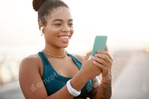 Preview: Dark-skinned woman smiling while using social media after running