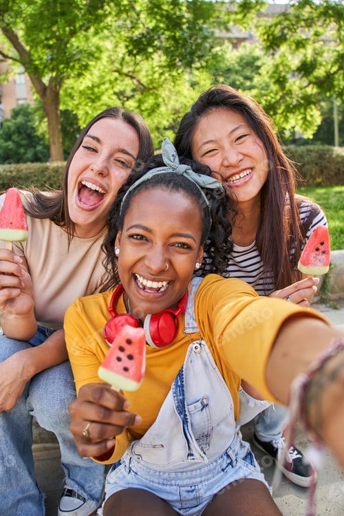Preview: Close up faces three smiling young multi-ethnic women outdoors eating ice cream. Concept friendship.