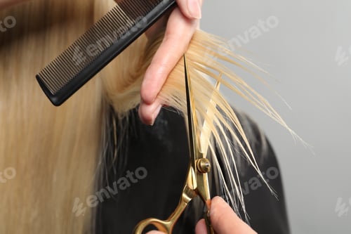 Preview: Hairdresser cutting client's hair with scissors on light grey background, closeup