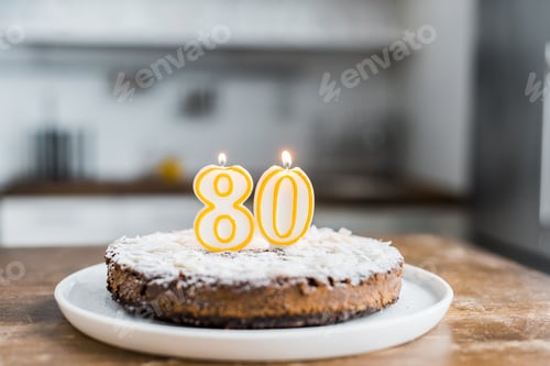 Preview: selective focus of delicious birthday cake with burning candles and '80' sign on top