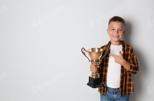 Preview: Happy boy with golden winning cup on light background. Space for text