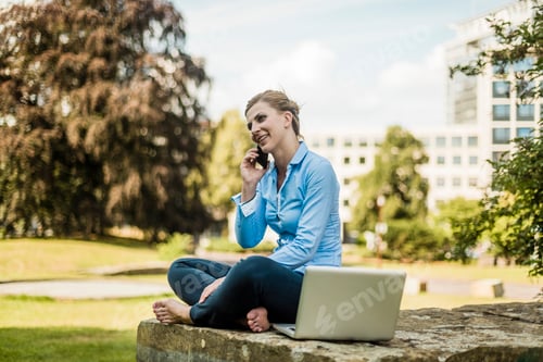 Preview: Smiling woman sitting in urban park talking on cell phone