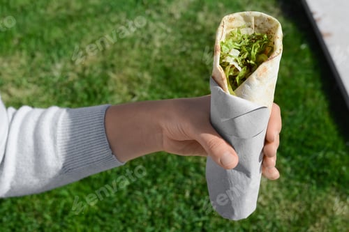 Preview: Woman holding delicious vegetable roll outdoors, closeup