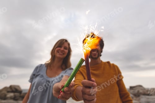 Preview: Young Caucasian couple playing with fire cracker while standing at beach.