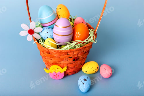 Preview: Close up of wicker basket filled with decorative multi colored eggs on a light blue background