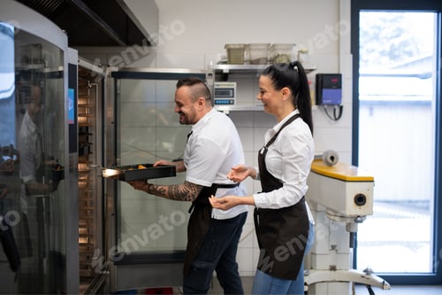 Preview: Happy chef and cook working on their dishes indoors in restaurant kitchen