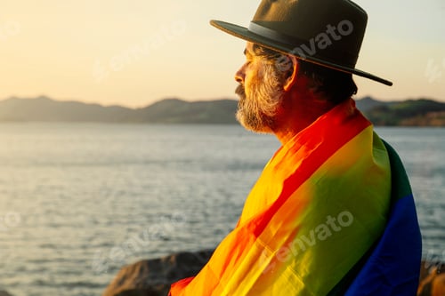 Preview: Portrait of a man with an lgtbi pride flag in the light of sunrise