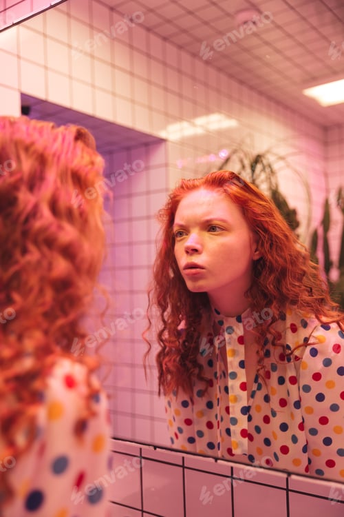 Preview: Concentrated young redhead curly lady looking at mirror.
