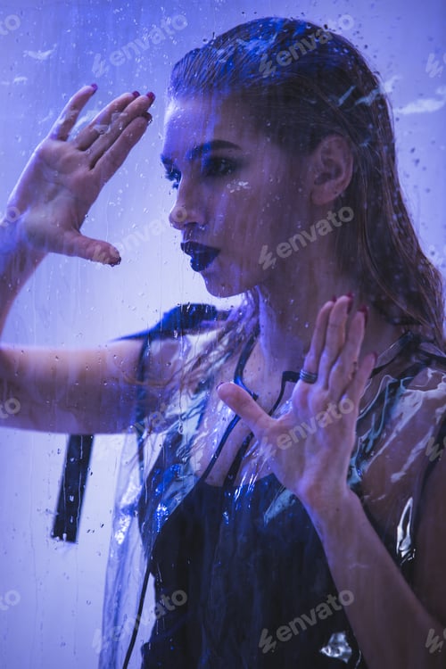 Preview: Fashionable model with wet hair dressed in black swimming suit and transparent rain coat is posing