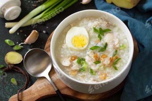 Preview: Arroz Caldo Soup. Hot soup with ginger chicken rice and garlic in a bowl on a dark countertop.