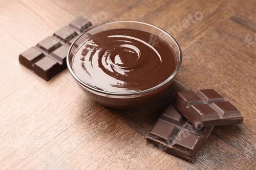 Preview: Bowl with melted chocolate and pieces on wooden table, closeup