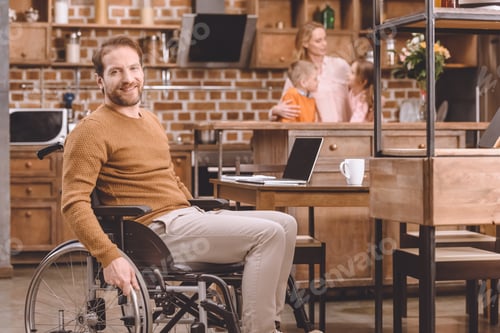 Preview: disabled middle aged man in wheelchair smiling at camera while spending time with family at home
