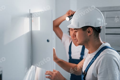 Preview: Two young male electricians works indoors together. Using flashlight