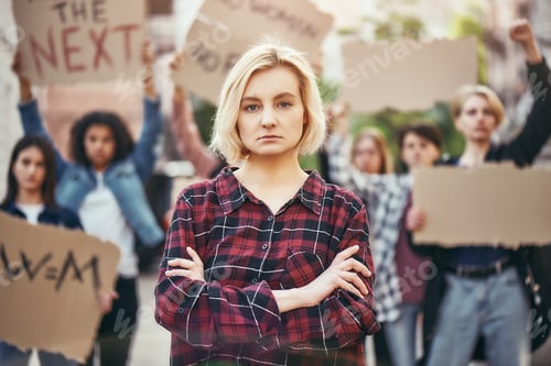 Preview: Fighting for my rights. Young blonde woman is standing with crossed arms during a protest in front