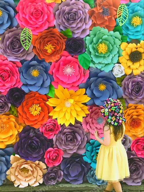 Preview: Toddler girl in a yellow dress and floral hat admiring a brightly colored wall of flowers