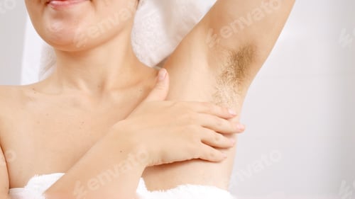 Preview: Closeup of long dark hair growing under arms of young woman standing at bathroom mirror