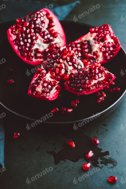 Preview: Close up view on a ripe pomegranate in a black plate on a dark background.