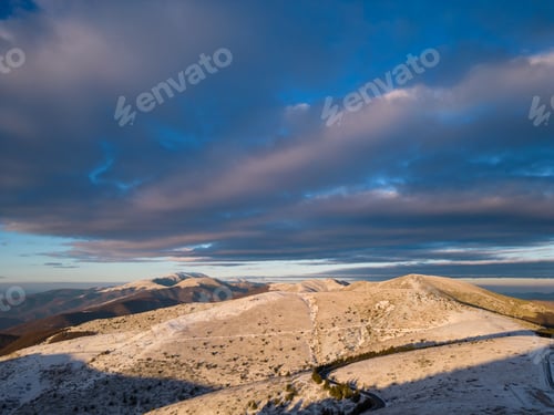Preview: snow covered mountains at sunset with a winding road in the foreground aerial view