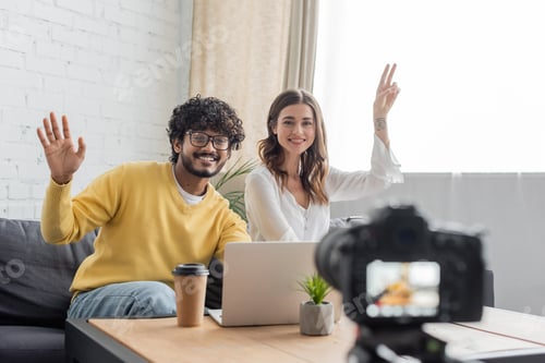 Preview: cheerful interracial vloggers in casual clothes waving hand and showing victory gesture