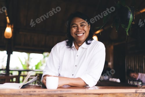 Preview: Cheerful Asian man laughing while sitting at table in cafe