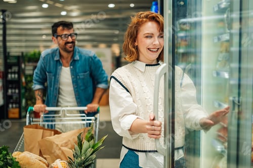 Preview: Happy couple shopping for groceries, opening refrigerator in supermarket
