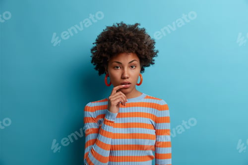 Preview: Calm beautiful woman with natural curly hair, looks with attentive focused expression, wears casual