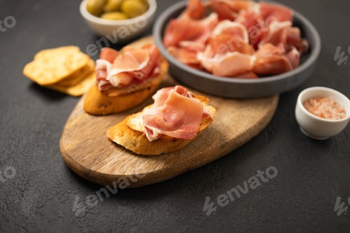 Preview: Italian sandwiches bruschetta with olives, bran bread, cherry tomatoes, prosciutto on wooden cutting