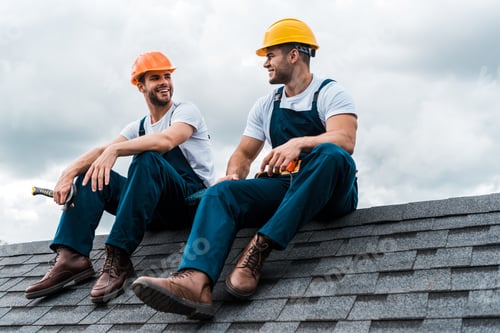 Preview: happy handymen in helmets and uniform sitting on rooftop